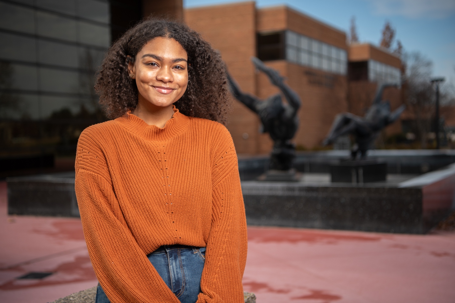 Young woman in orange sweater with Night and Day Fountain in background